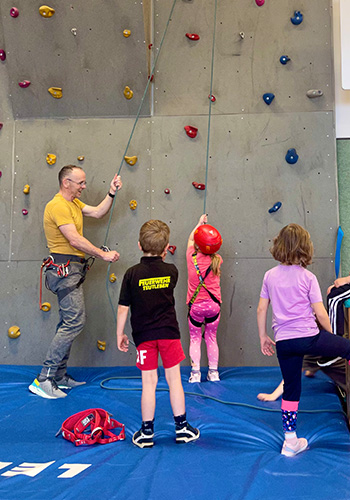 Trainer und Kinder vor Kletterwand mit Bouldergriffen